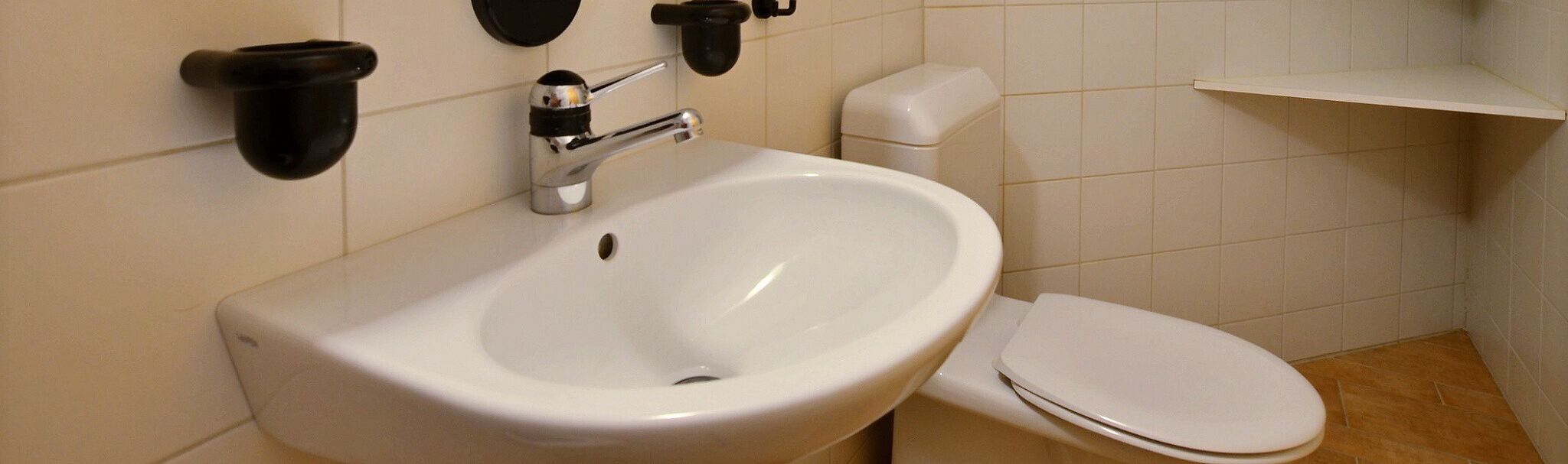 Une salle de bain avec un lavabo blanc, des toilettes et un distributeur de savon fixé au mur.