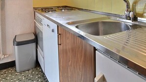 Kompakti keittiö, jossa on ruostumattomasta teräksestä valmistettu pesuallas, pieni roskakori ja liesi.