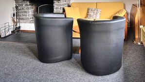 Huoneessa on keltainen sohva, kaksi mustaa sylinterinmuotoista jakkaraa, takka ja ikkuna, josta avautuu näkymä puiseen terassille.
