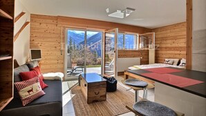 A modern room with wooden walls, a sofa with red and white cushions, a small table, and a view of mountains through large windows.