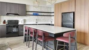 A modern kitchen with a central island, bar stools, a built-in oven, and a refrigerator.