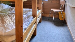 A bunk bed with a wooden frame and a mattress. There is a chair and a yellow bucket against the wall. - Middle class flat for 5 people, living room with fireplace, kitchen area with dishwasher, 1 bedroom (Grimentz)