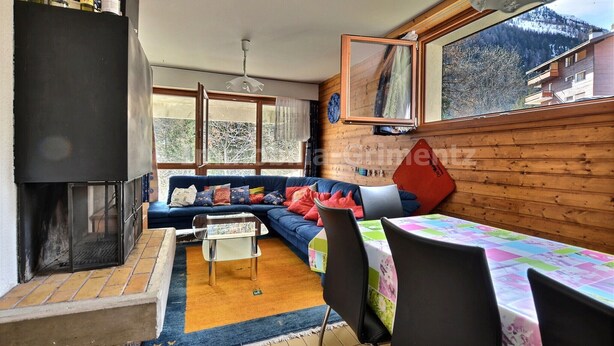 A cozy living room with a fireplace, a sofa, a dining table, and a view of a mountain. - Middle class flat for 5 people, living room with fireplace, kitchen area with dishwasher, 1 bedroom (Grimentz)