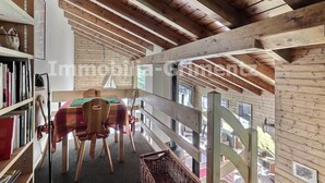 Un interior de madera con una mesa y sillas de comedor, estanterías y vistas por una ventana.