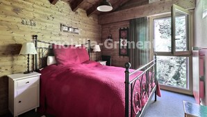 Un dormitorio de cabaña de madera con una cama, mesitas de noche, una ventana y vistas a árboles.