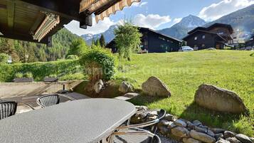 Ein Sitzbereich im Freien mit Tisch und Stühlen, einer Steinmauer und einem Blick auf Berge und Gebäude im Hintergrund.