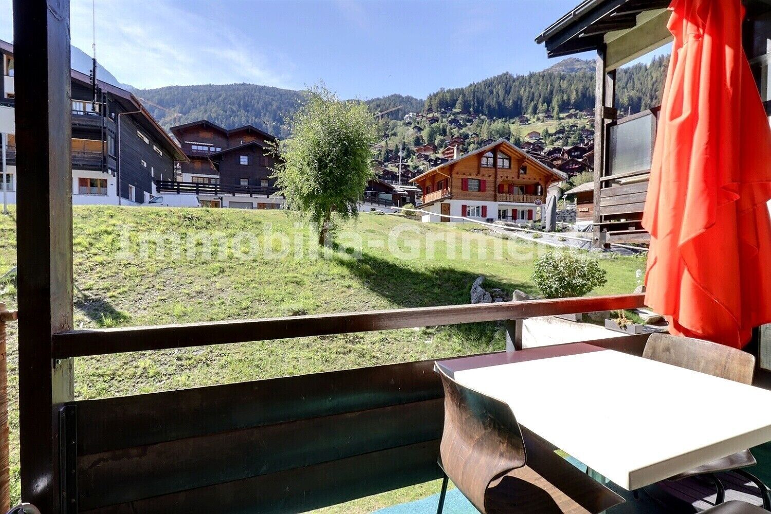 A balcony with a table and chairs, overlooking a village with traditional houses and a mountain in the background.
