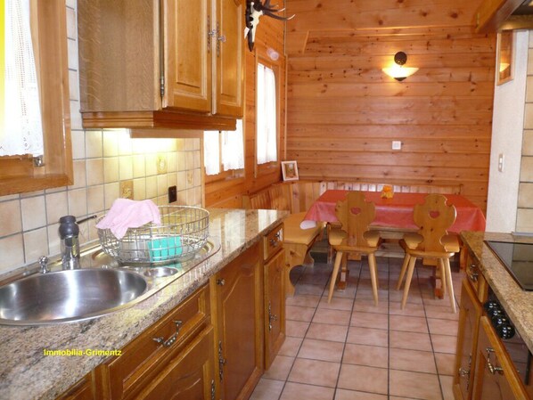A wooden kitchen with a sink, cabinets, and a dining area with chairs and a table.