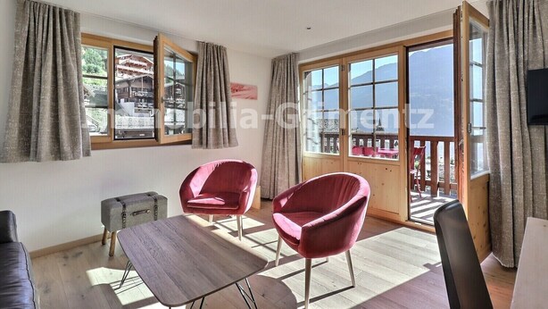 Une pièce avec deux chaises rouges, une petite table et un balcon doté d’une balustrade en bois.