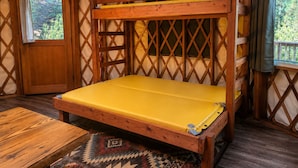 Un lit superposé en bois avec un matelas jaune, dans une chambre rustique aux murs en bois et dotée d’une fenêtre.