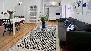 Ein modernes Wohnzimmer mit einer Couch, einem Esstisch mit Stühlen, einem Couchtisch, einer Treppe und einer Wand mit gerahmten Kunstwerken.