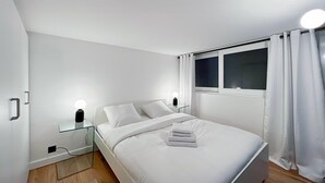 Ein modernes Schlafzimmer mit einem Einzelbett, Nachttischen mit Lampen, einem Vorhangfenster und Holzboden.
