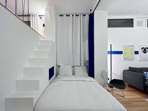 A modern bedroom with a bed, a chair, a staircase, and a wall with two framed pictures. - Cosy T3 in the heart of Popincourt (Paris)