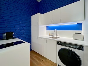 A modern kitchen with white cabinets, a built-in dishwasher, and a blue accent wall. - Cosy T3 in the heart of Popincourt (Paris)
