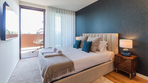 A bedroom with a large bed, a nightstand with a lamp, a chair by the window, and a view of the outside balcony. - Contemporary Oasis w/ Balcony by LovelyStay (Vila Nova de Gaia)