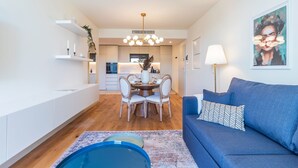 A modern living room with a blue sofa, a dining area with a wooden table and chairs, and a kitchen in the background. - Contemporary Oasis w/ Balcony by LovelyStay (Vila Nova de Gaia)