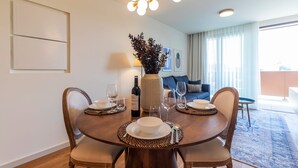 A dining area with a round table set for four, a vase with dried plants, and a bottle of wine. - Contemporary Oasis w/ Balcony by LovelyStay (Vila Nova de Gaia)