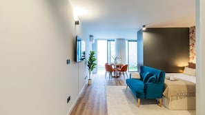 Un salon moderne avec un canapé, une table à manger et des chaises, une plante en pot et un téléviseur fixé au mur.