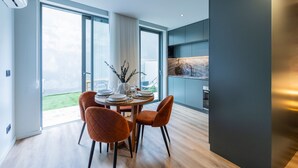 A modern dining area with a round table, two velvet chairs, and a view of a green outdoor space through large windows. - RUAH C - Cozy Studio by LovelyStay (Vila Nova de Gaia)