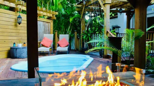 Une terrasse en bois avec un foyer en verre, une petite piscine et deux chaises dotées de coussins rouges.