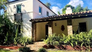 Une maison à deux étages avec un balcon, des marches en briques et un jardin où poussent différentes espèces de plantes.