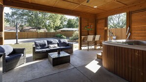 An outdoor patio area with wicker furniture, a hot tub, and a wooden ceiling.