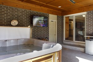 Un espace détente avec un jacuzzi, un téléviseur diffusant une chaîne de sport et un mur en briques.