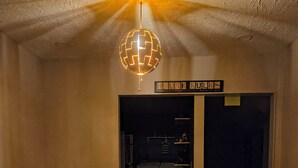 Un coin repas avec une table et des chaises en bois, un luminaire suspendu en forme de globe et une cuisine visible à travers une porte ouverte.