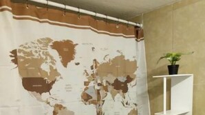 Une salle de bain avec un rideau de douche orné d’une carte du monde, une étagère blanche sur laquelle est posée une plante en pot, et une pancarte indiquant « Style Bespin ».