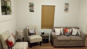 Un salon comprenant un canapé, deux fauteuils, une petite table et une fenêtre avec des stores.