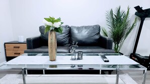 A modern living room with a glass coffee table, a decorative vase, a guitar, and a remote control. - AviAana 1 Bedroom Basement Suite (Edmonton)