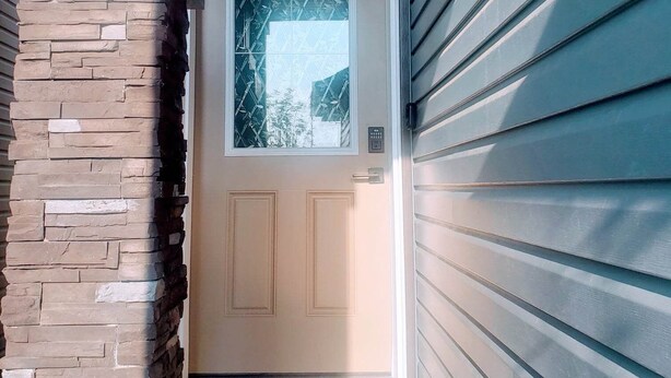 A house entrance with a stone pillar, a glass door, and a doormat. - AviAana 1 Bedroom Basement Suite (Edmonton)