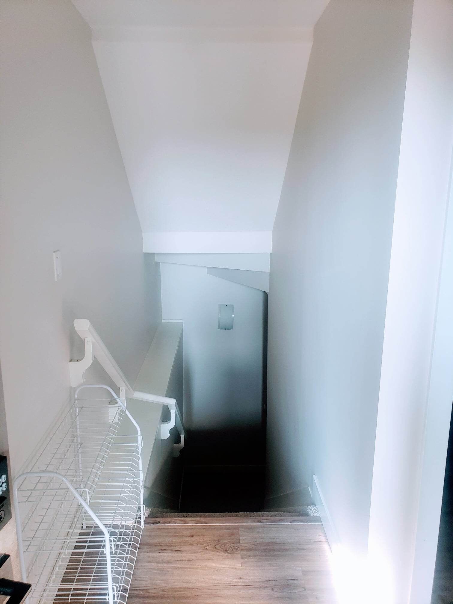 A narrow stairway leading to a dark room with a white wall and a metal shelf on the left.