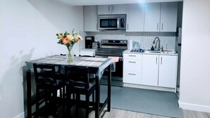 A compact kitchen with a microwave, stove, and sink. There is a table with chairs and a vase of flowers. - AviAana 1 Bedroom Basement Suite (Edmonton)