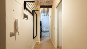 Un couloir étroit, avec une porte blanche au fond, un téléphone fixé au mur et un luminaire au plafond.