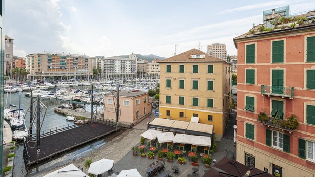Un port de plaisance avec des bateaux, un bâtiment jaune avec des volets verts et un bâtiment rouge avec des balcons.