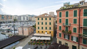 Un port de plaisance avec des bateaux, un bâtiment jaune aux volets verts et des tables à l’extérieur, protégées par des parasols.