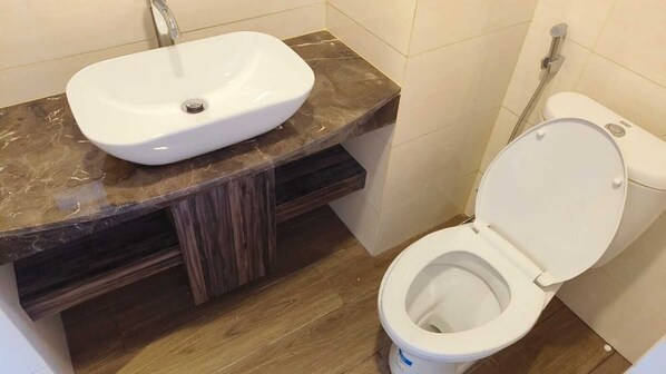 A bathroom with a white sink on a marble countertop, a toilet with a white lid, and wooden cabinetry.