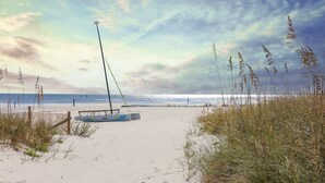 Ein Strand mit einem Segelboot, Sanddünen und einem bewölkten Himmel.
