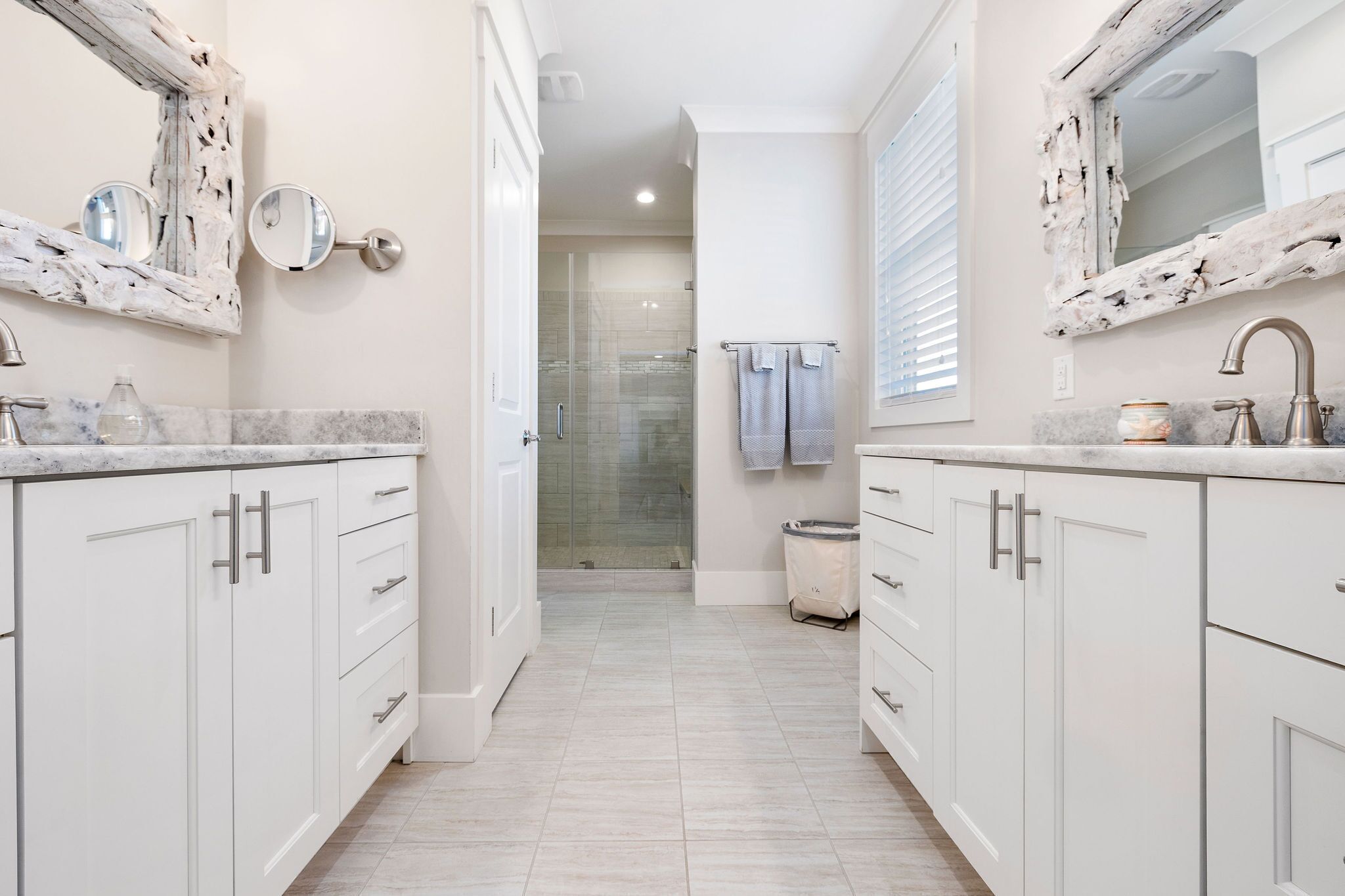 A modern bathroom with white cabinetry, marble countertops, and a glass shower enclosure.