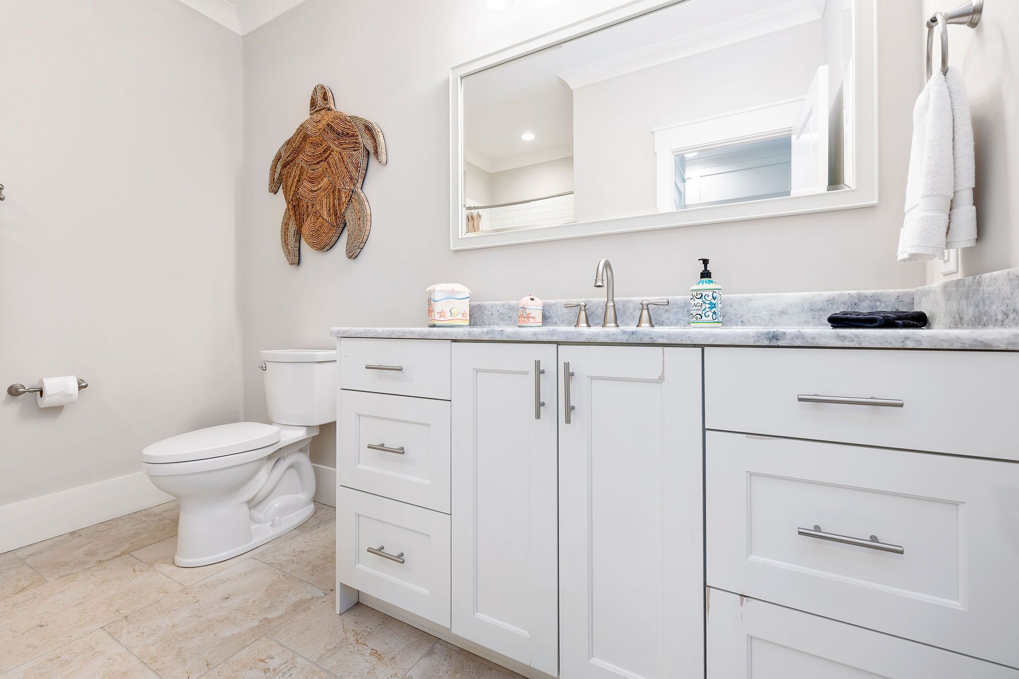 A modern bathroom with a toilet, a sink with a marble countertop, and a large mirror.