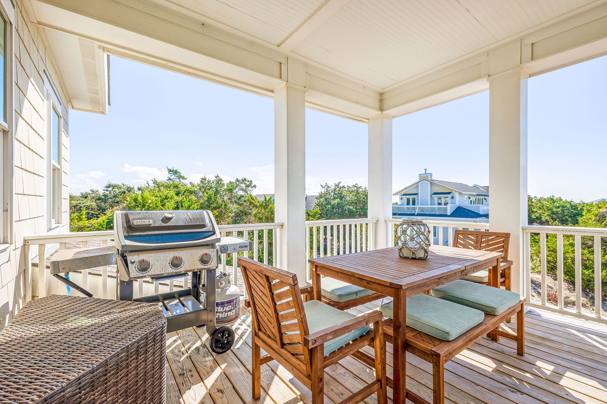 A covered outdoor deck with a grill, wooden table, and chairs.