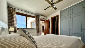 Une chambre à coucher comprenant un lit, un ventilateur de plafond, une fenêtre avec des rideaux et une armoire.