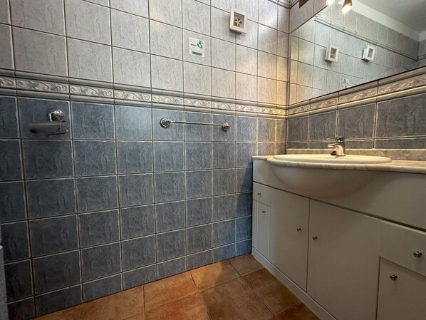 Une salle de bain avec des murs recouverts de carreaux gris, un lavabo blanc et un miroir.