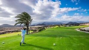 Un parcours de golf offrant une vue dégagée sur le paysage environnant, notamment sur les montagnes et un ciel clair.