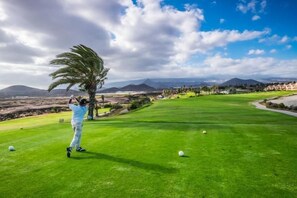 Ein Golfplatz mit freiem Blick auf die umliegende Landschaft, darunter Berge und ein klarer Himmel.