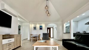 Un salon moderne avec une table basse en bois, un canapé en cuir noir, un téléviseur fixé sur un meuble et un coin repas comprenant une table et des chaises.