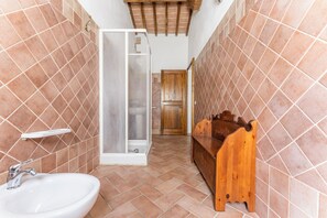 A bathroom with a white sink, wooden bench, and a shower area with a glass door. - Podere Marcigliana  (Radicondoli)