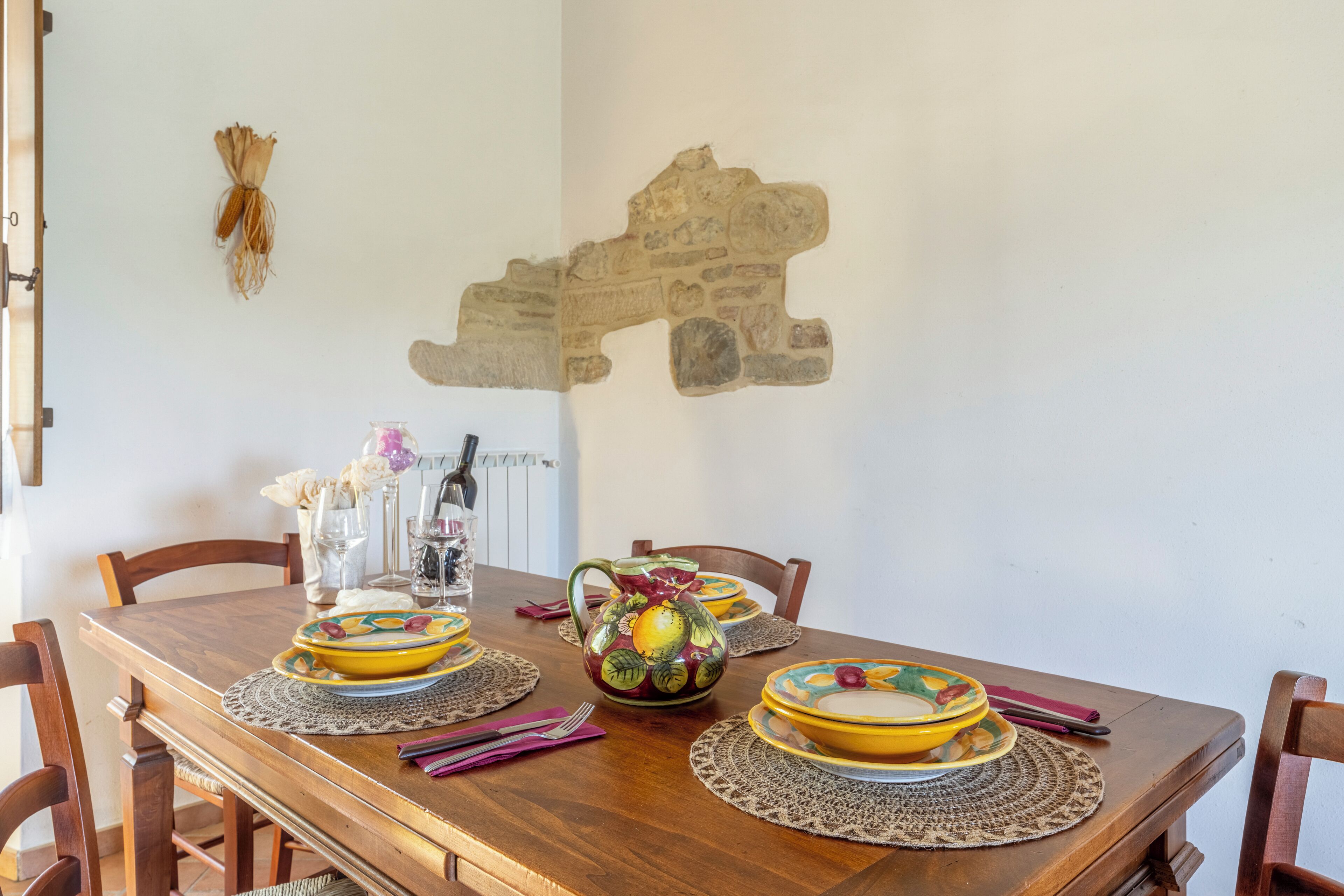 A wooden dining table with yellow plates, a pitcher, and a vase with flowers.