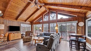 A spacious living room with wooden floors, a large sofa set, a TV, and a dining area with a table and chairs. - 4BR Lakehouse | Sleeps 10 | Fire Pit, Dock, Kayaks (Long Pond)